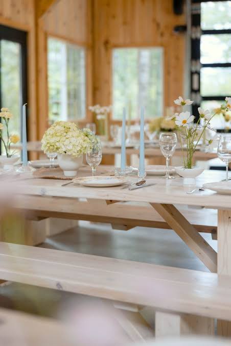 Light-wood farm tables set with candles and white florals inside the cottage